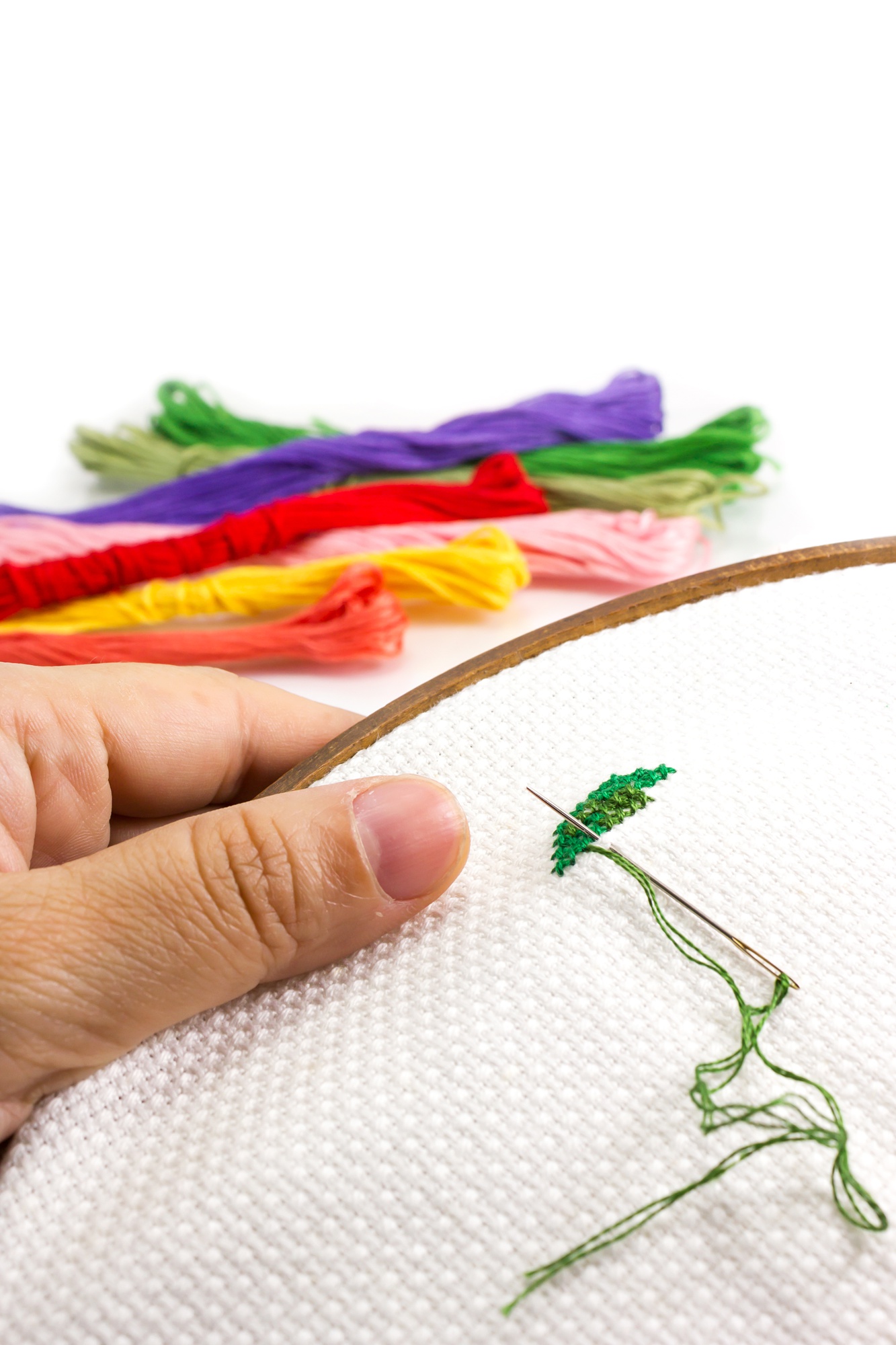Hands threading a needle over colorful embroidery